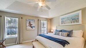 A bedroom with a large bed, a ceiling fan, a bench, and a painting on the wall. - Orange Beach Home w/ Hot Tub < 2 Mi to The Wharf (Orange Beach)
