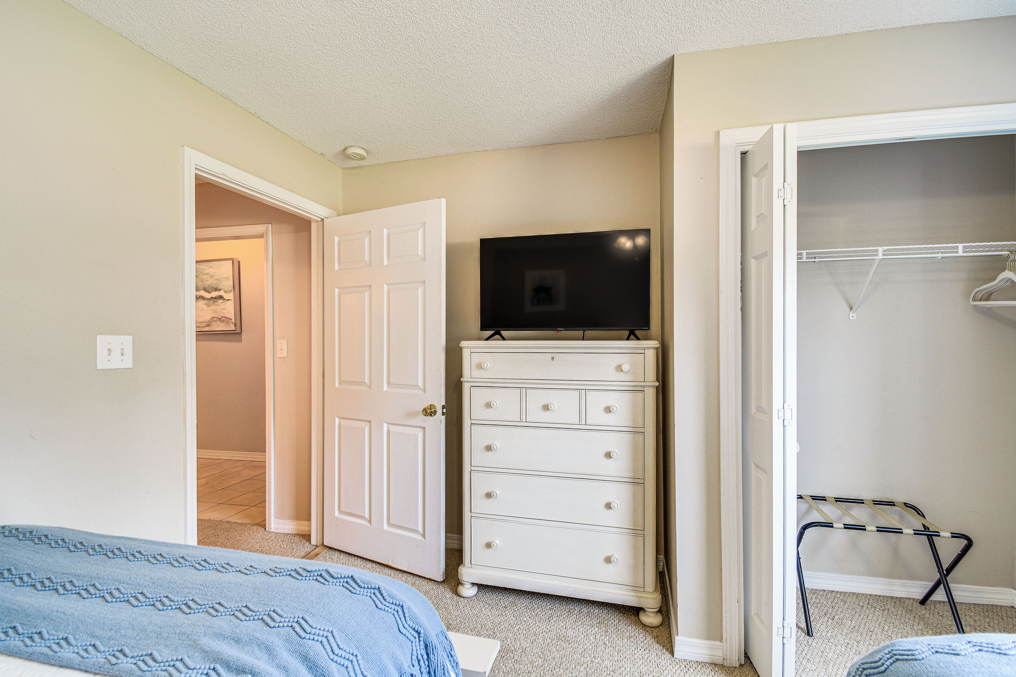 A bedroom with a bed, a dresser, a television on top, and a closet with a hanging rod.