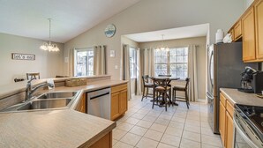 A modern kitchen with a built-in dishwasher, stainless steel sink, wooden cabinets, a dining area with a table and chairs, and a refrigerator. - Orange Beach Home w/ Hot Tub < 2 Mi to The Wharf (Orange Beach)