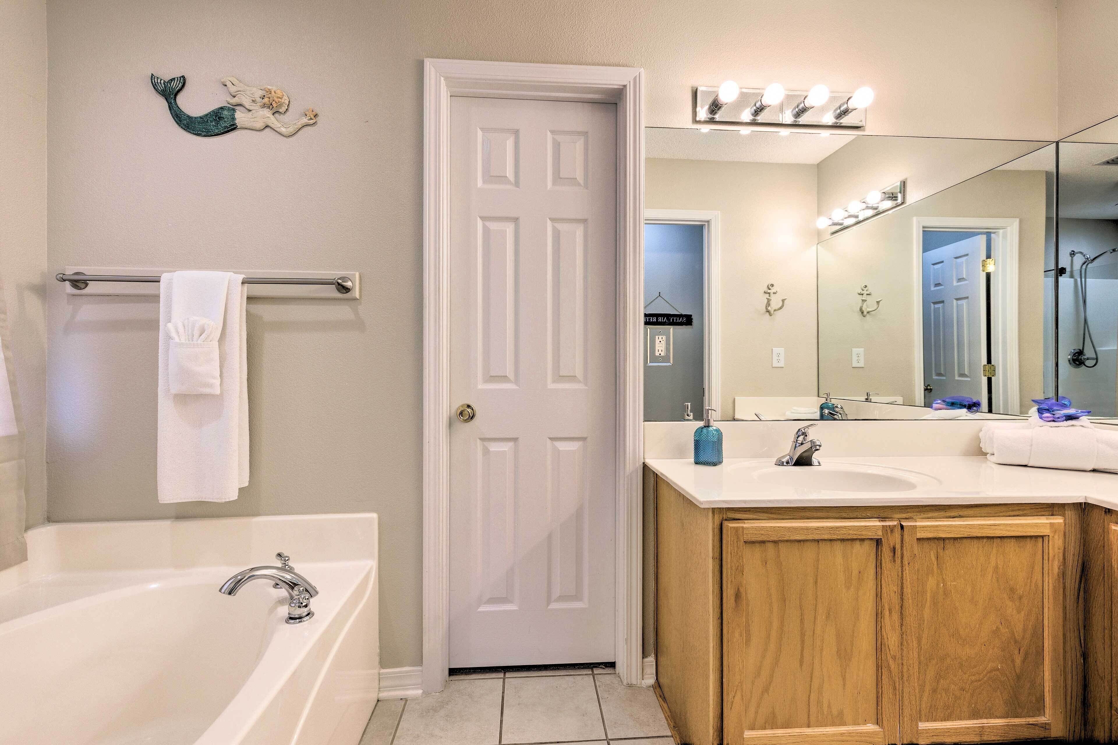 A bathroom with a white bathtub, wooden vanity, and a large mirror with lights.