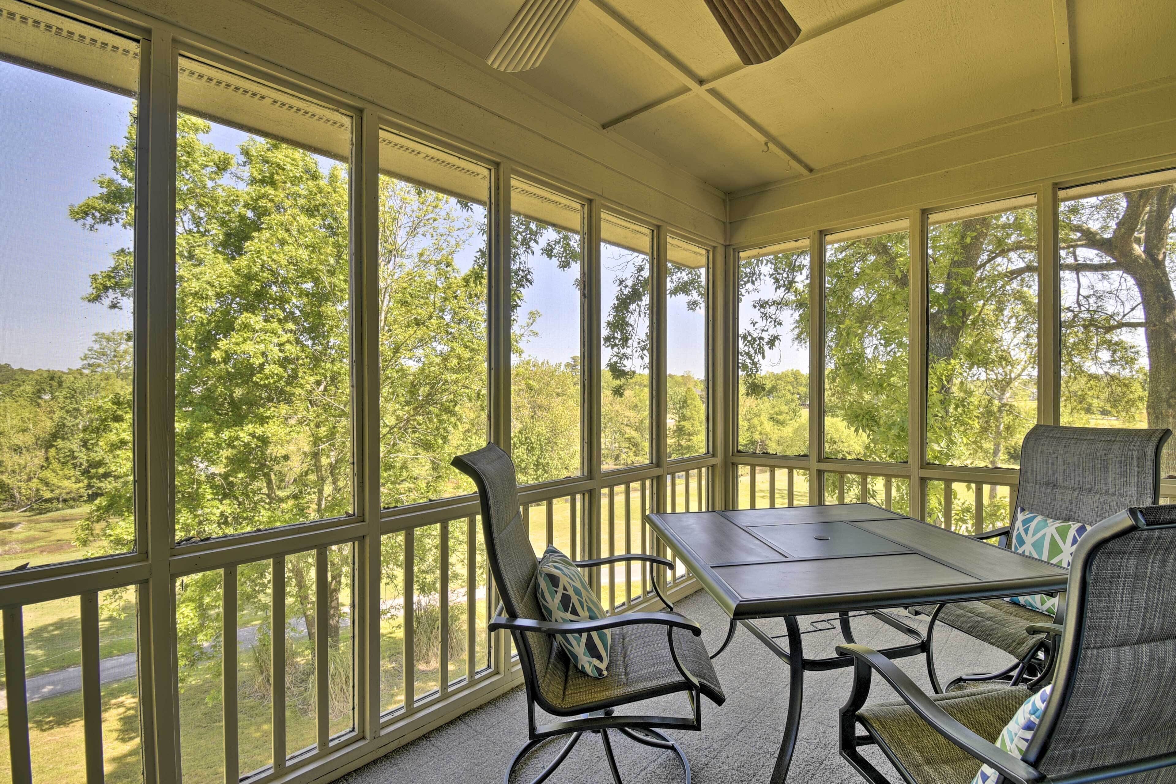 A covered patio with a table and chairs, large windows, and a view of trees.