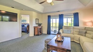 A living room with a ceiling fan, a large TV, a sofa, a coffee table, and a window with curtains. - Sea Trail Resort Villas Condo w/ Community Perks! (Sunset Beach)