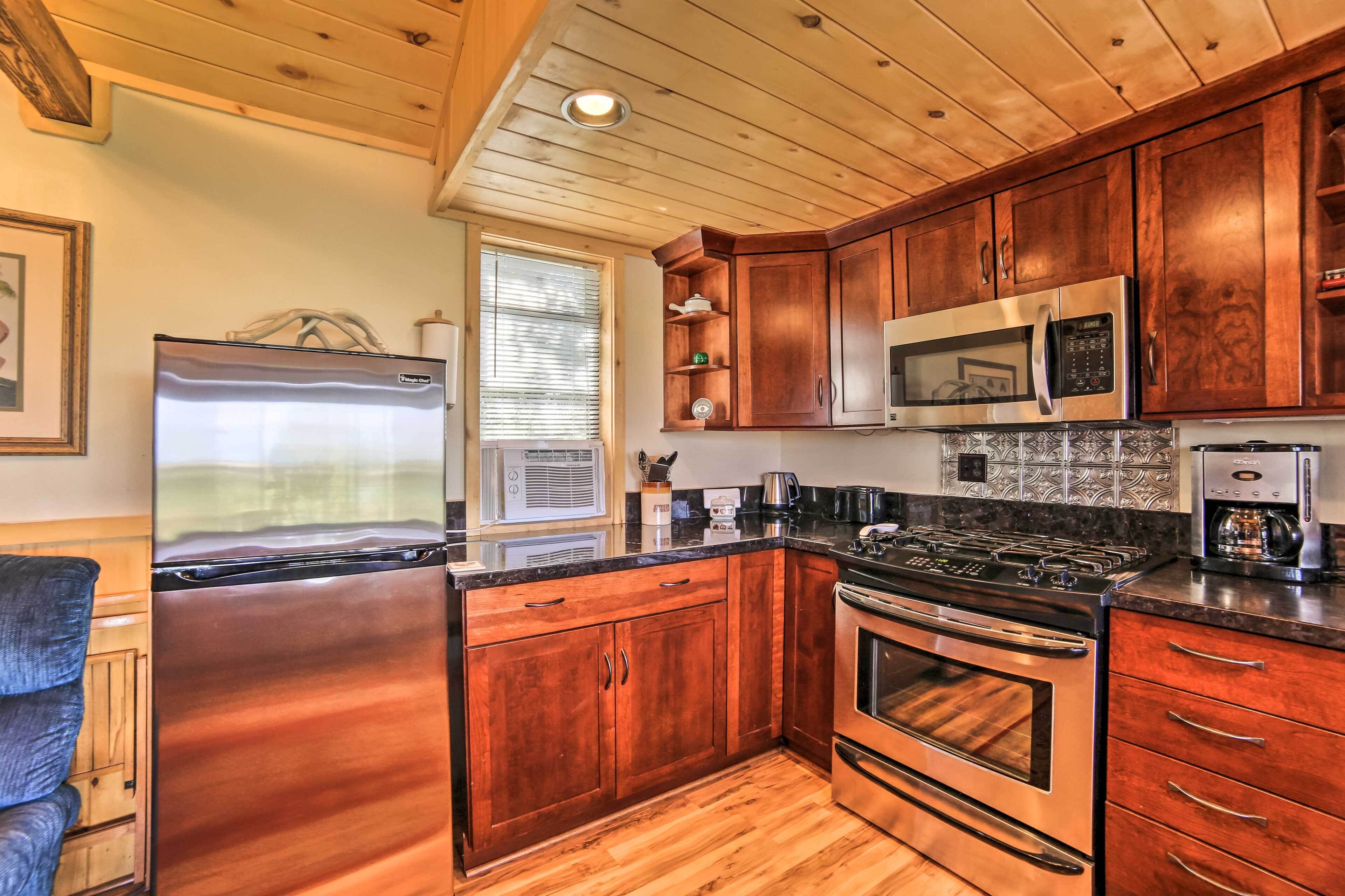 A kitchen with wooden cabinets, a stainless steel refrigerator, a microwave, a stove, and a coffee maker.
