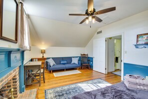 A room with a wooden floor, a blue sofa, a wooden chair, a table, a fireplace, and a ceiling fan. - Idyllic Appomattox Home w/ Porch & Rocking Chairs! (Appomattox)