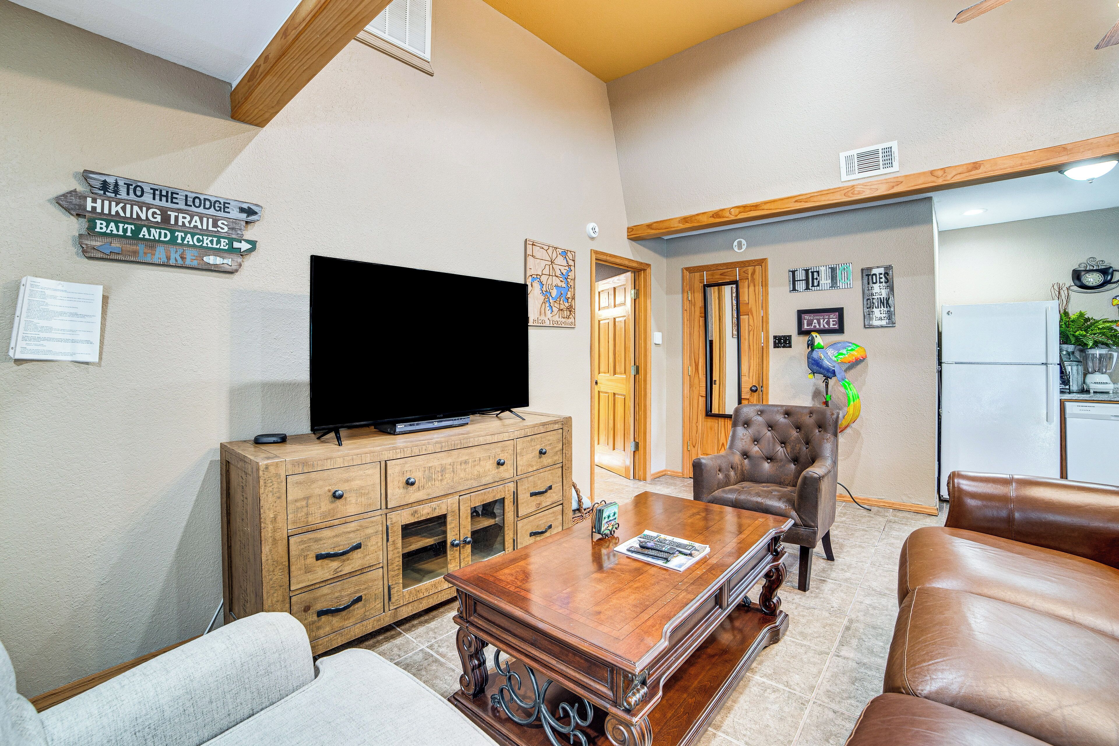 A living room with a television, wooden cabinet, leather sofa, and a coffee table. There are signs on the wall indicating hiking trails and bait and tackle.