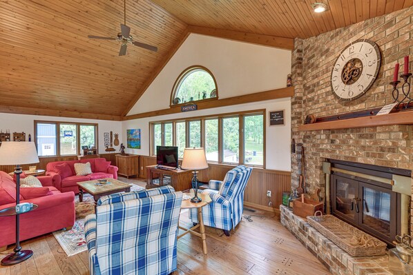 A spacious living room with a fireplace, wooden ceiling, and large windows. - Private Dock & Stunning Views: Corey Lake Getaway! (Three Rivers)