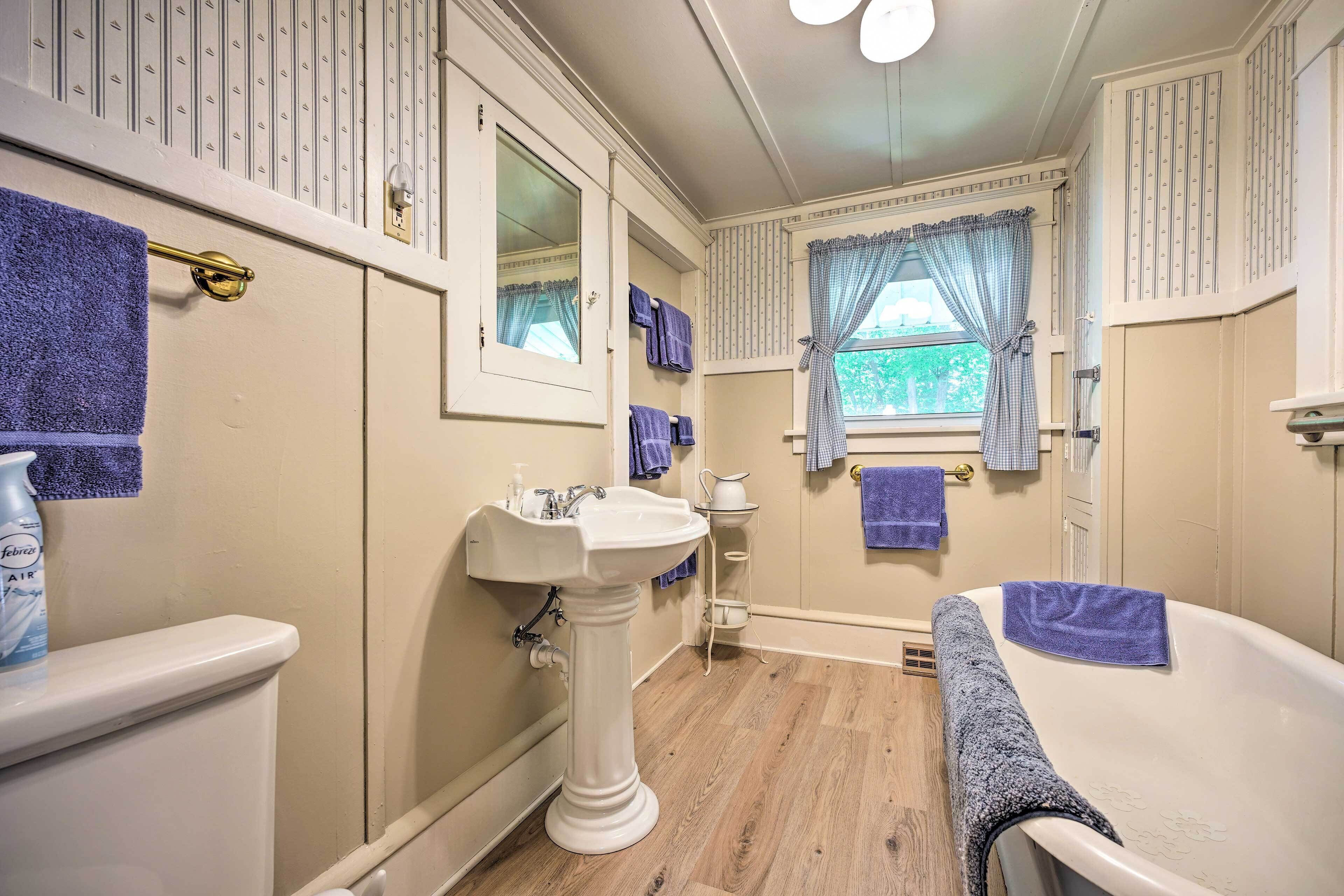 Une salle de bain avec un lavabo sur colonne, une baignoire et une fenêtre avec des rideaux.