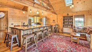 A rustic cabin interior with a wooden bar, stools, a patterned rug, and a cozy seating area. - Lakefront Cottage: Boat Dock, Patio & Kayaks! (Oxford)