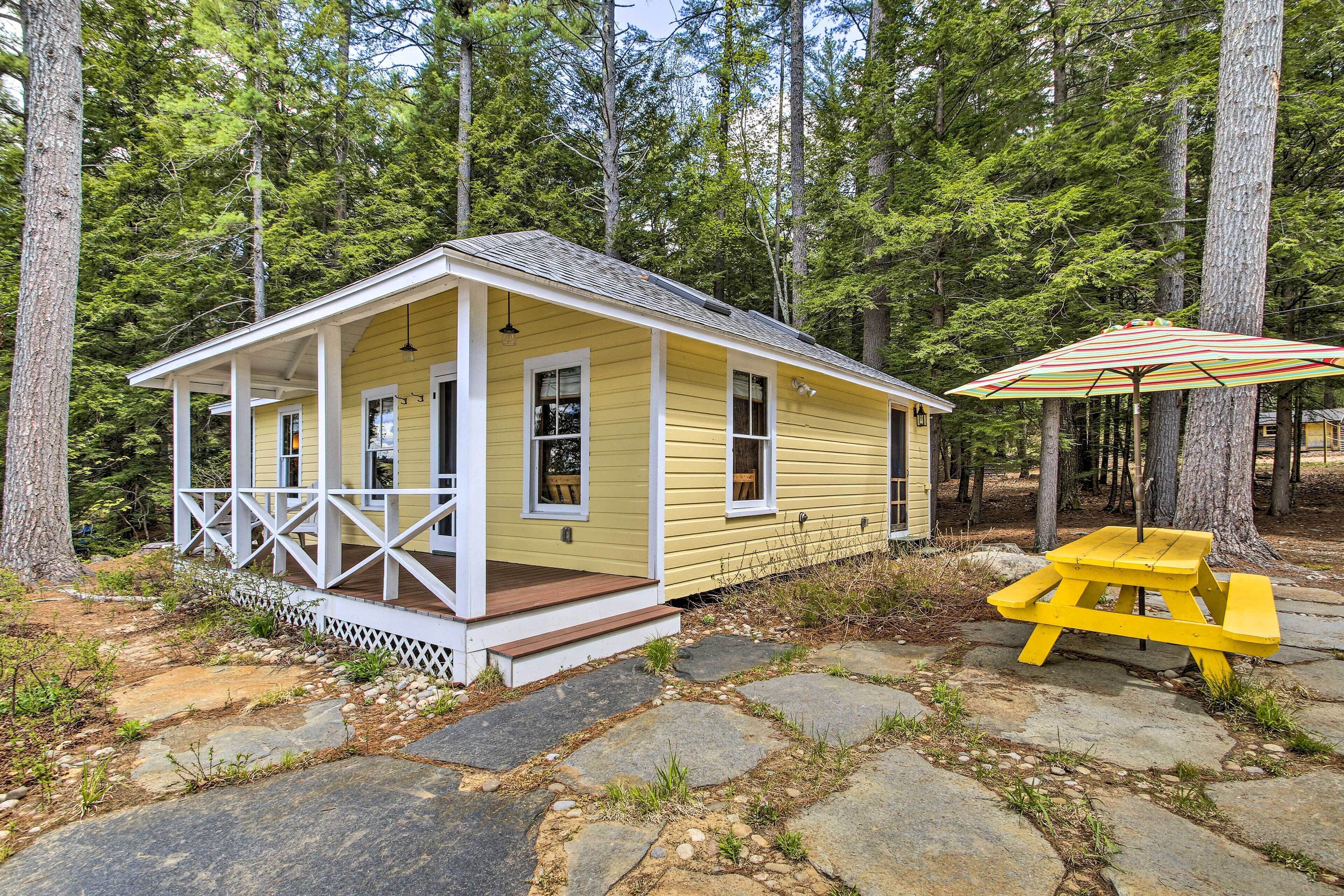 A yellow cabin with a porch and a picnic table with an umbrella.