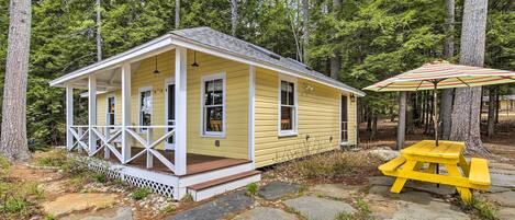 A yellow cabin with a porch and a picnic table with an umbrella.