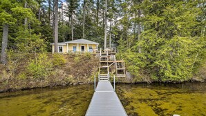 A wooden dock leading to a house surrounded by dense forest. - Lakefront Cottage: Boat Dock, Patio & Kayaks! (Oxford)
