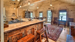 A rustic cabin interior with a wooden bar, seating area, and large windows. - Lakefront Cottage: Boat Dock, Patio & Kayaks! (Oxford)