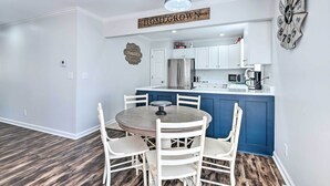 Una cocina moderna con armarios blancos, una isla azul y una zona de comedor con una mesa redonda y sillas blancas.