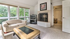 A living room with a beige sofa, a leather ottoman, a fireplace, and a television. - Lake Harmony Villa: Walk to Big Boulder Mountain! (Lake Harmony)