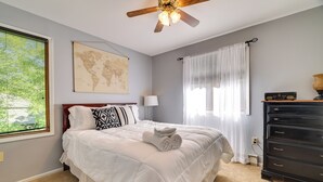 Une chambre à coucher avec un lit, une carte du monde accrochée au mur, un ventilateur de plafond et une commode.