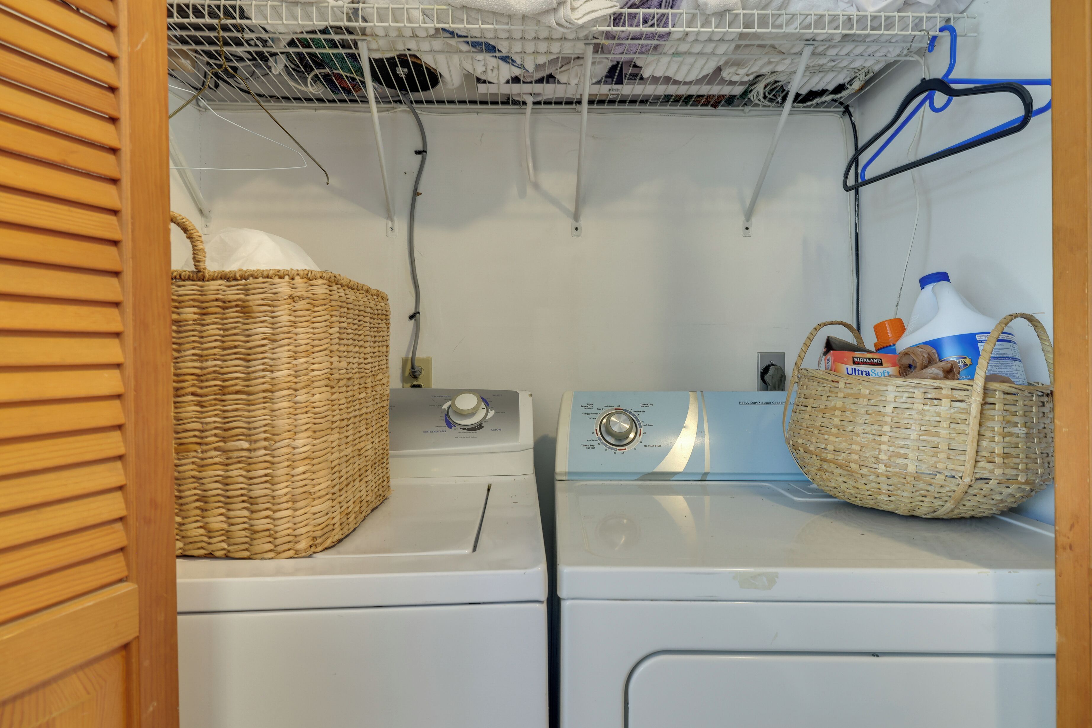 A laundry area with a front-loading washer and dryer, baskets, and a hanging rack.