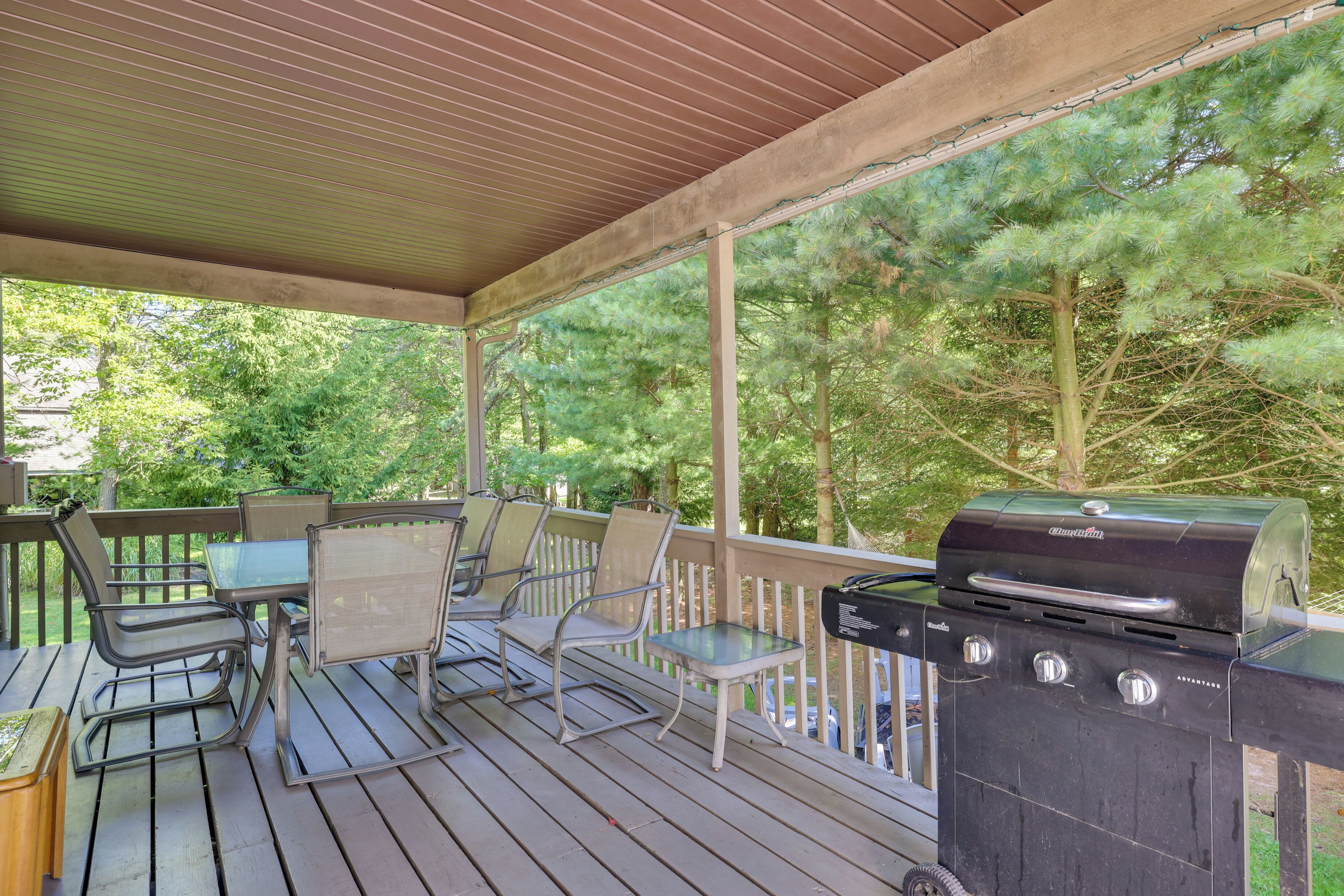 A covered outdoor deck with a grill, chairs, and a table.