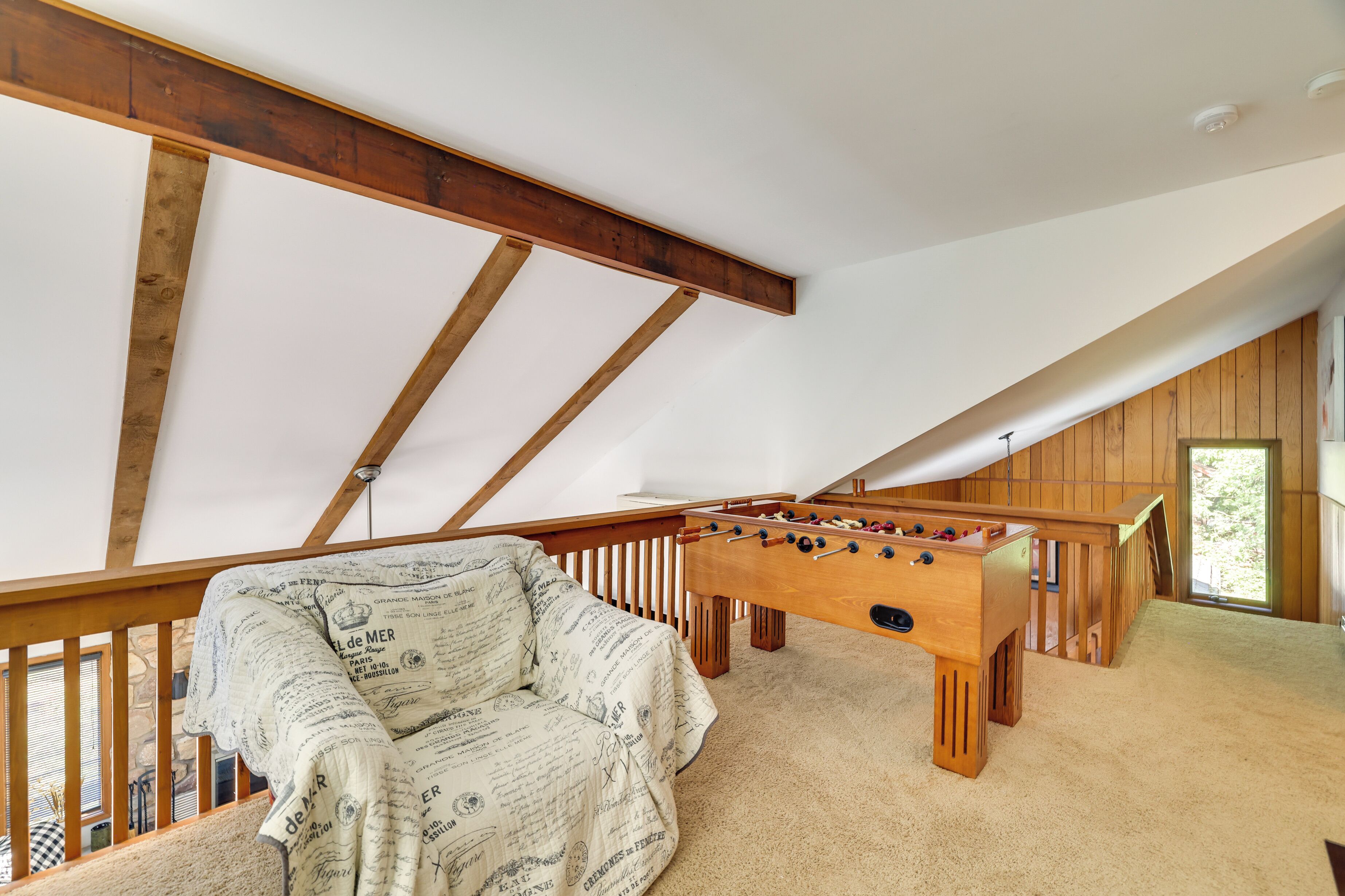 Une chambre à coucher confortable, aménagée en mezzanine, avec un plafond en bois, une table de baby-foot et un canapé à motifs.