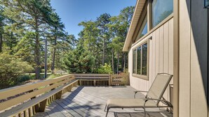 Une terrasse en bois avec un banc et un fauteuil de relaxation, entourée d’arbres et d’une maison.