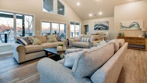 A spacious living room with multiple sofas, a coffee table, and large windows offering a view of the outdoors.