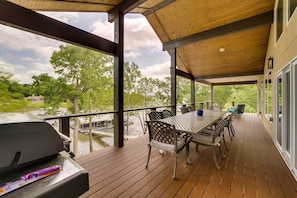 Een overdekt terras buiten, met een barbecue, eettafel en stoelen.