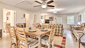 A dining area with a wooden table and chairs, a ceiling fan, and a kitchen in the background.
