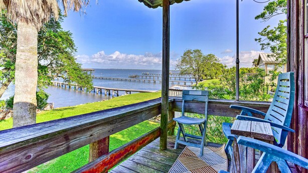 A wooden deck with chairs and a table overlooking a body of water with a pier.