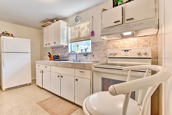 A kitchen with white cabinets, a built-in oven, a sink, and a window with blinds.