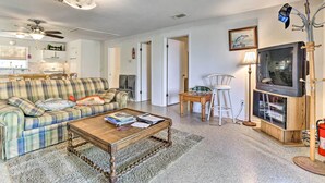 A living room with a plaid sofa, a wooden coffee table, a television on a wooden stand, and a ceiling fan.