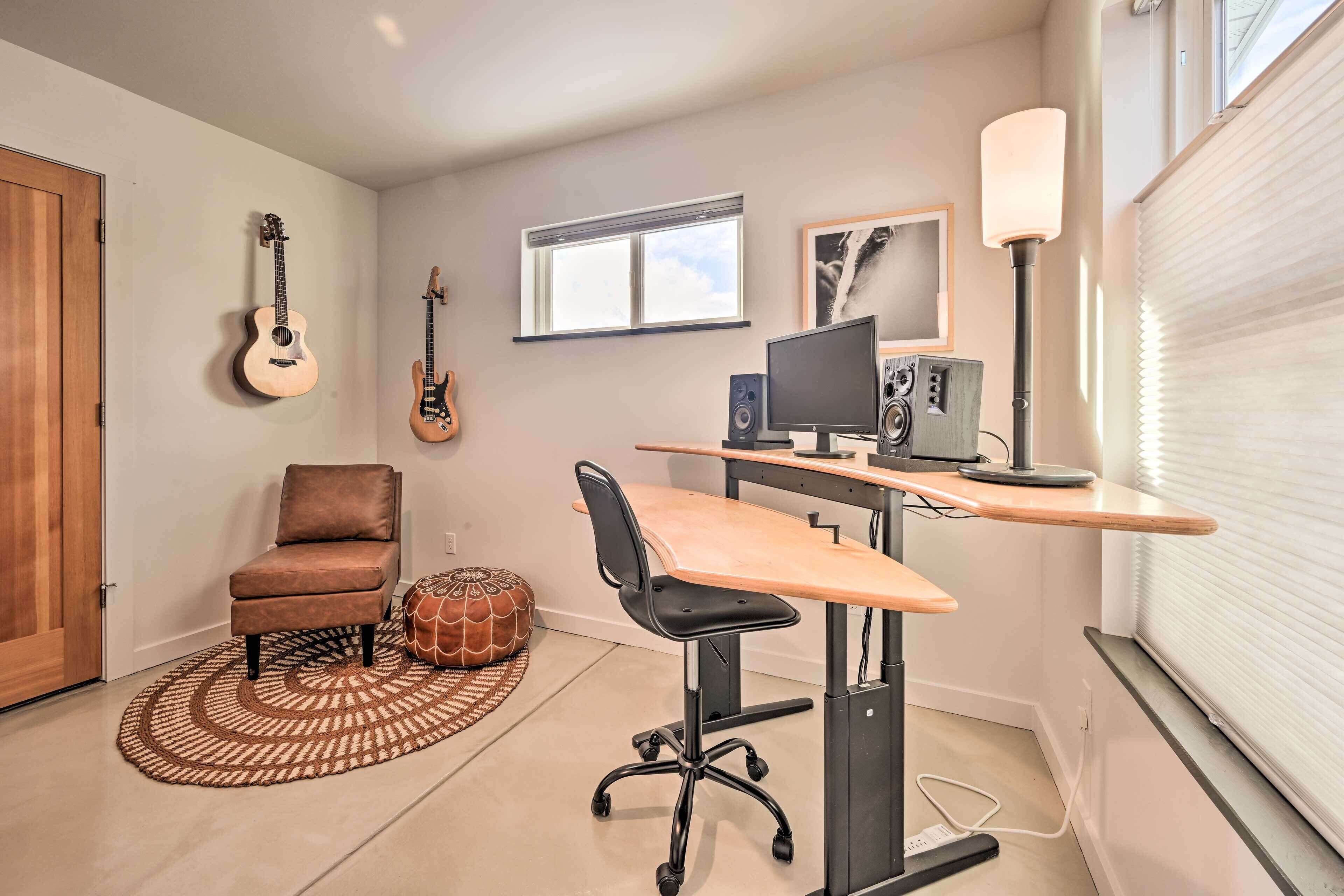 Una habitación con escritorio, silla, dos guitarras, una computadora y una lámpara.