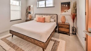 A bedroom with a large bed, two bedside tables, a nightstand, a wooden dresser, and a window with blinds. - Modern Missoula Home ~ 2 Miles to Downtown! (Missoula)