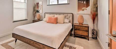A bedroom with a large bed, two bedside tables, a nightstand, a wooden dresser, and a window with blinds.