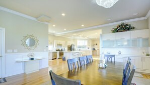 A spacious dining area with a wooden table and chairs, a kitchen in the background, and a chandelier. - Luxe Federal Way Rental - Walk to the Water! (Federal Way)