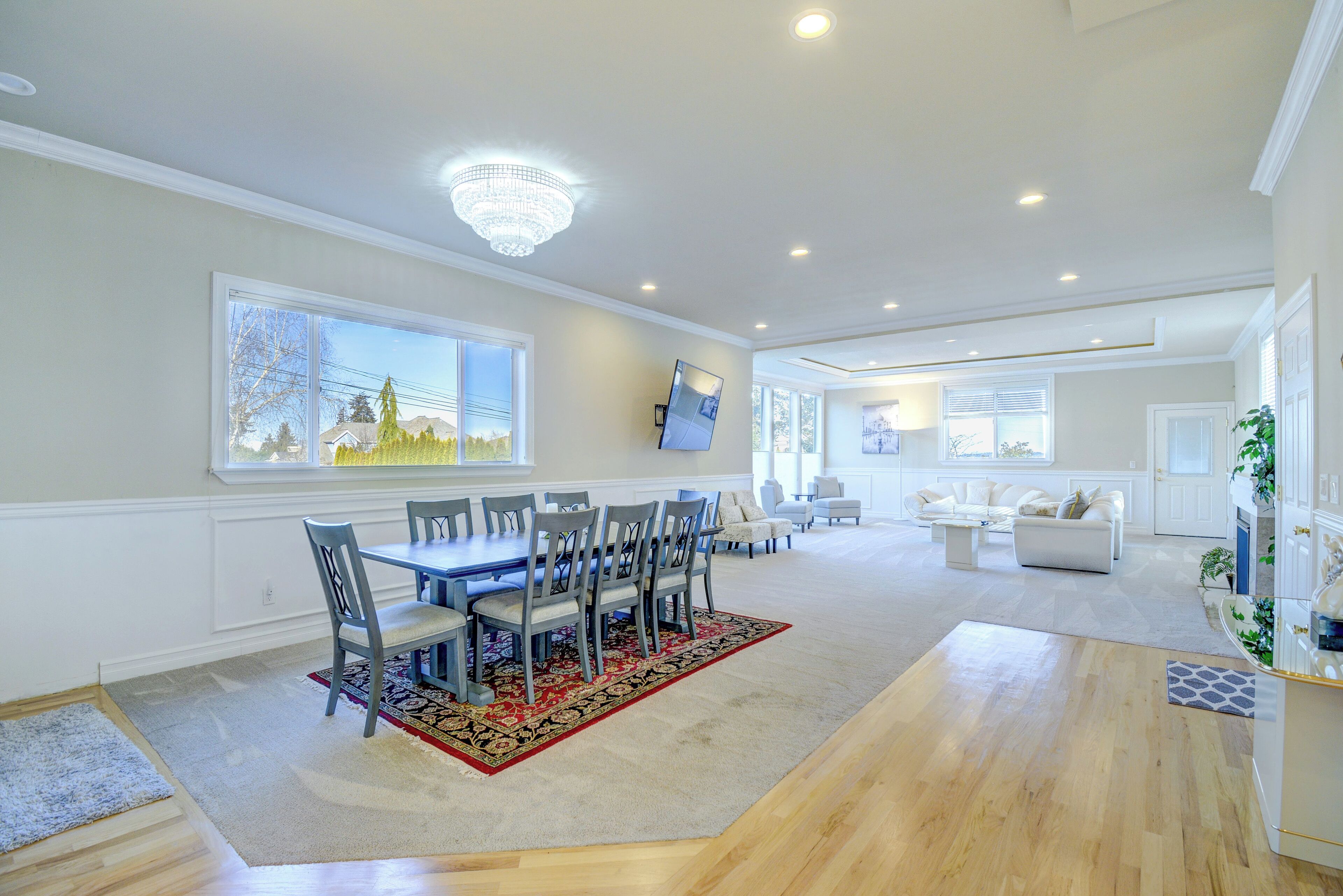 A spacious living room with a dining area, large windows, and a chandelier.