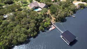 Una vista aerea di una casa con un molo che si protende in un lago, circondata da alberi rigogliosi.