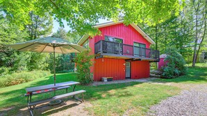 Een rode, twee verdiepingen tellende woning met een balkon, een picknicktafel en een parasol in een weelderige groene achtertuin.
