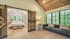 Una habitación con cama, sofá, lámpara y ventanas amplias.
