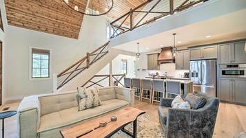 A spacious living area with a high ceiling, wooden beams, and a kitchen with stainless steel appliances.