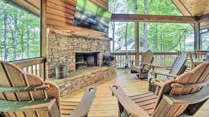 Una terraza de madera con sillas Adirondack, una chimenea de piedra y un televisor de pantalla plana montado encima.