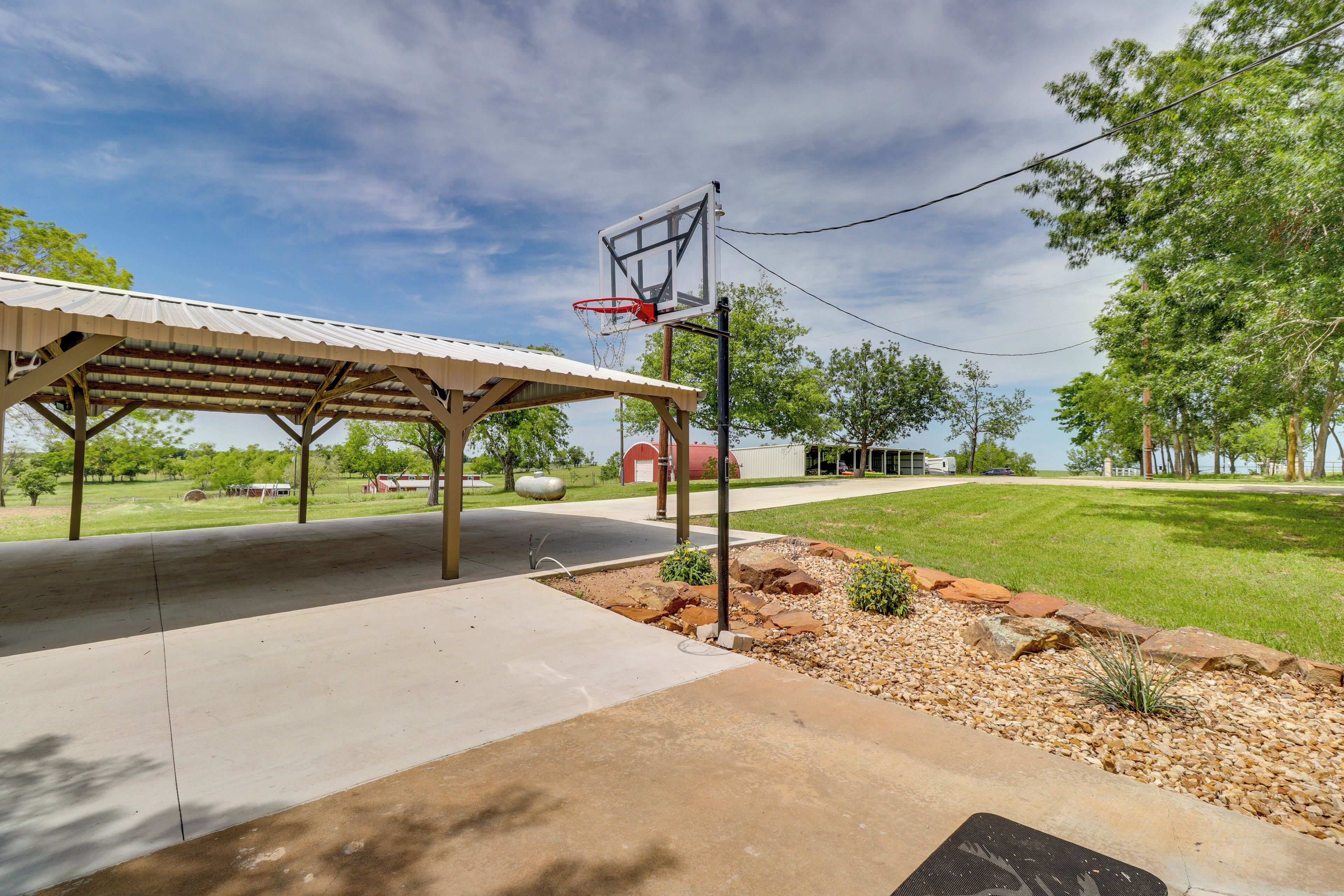 Una cancha de baloncesto con aro, una zona de estar cubierta y un césped bien cuidado.