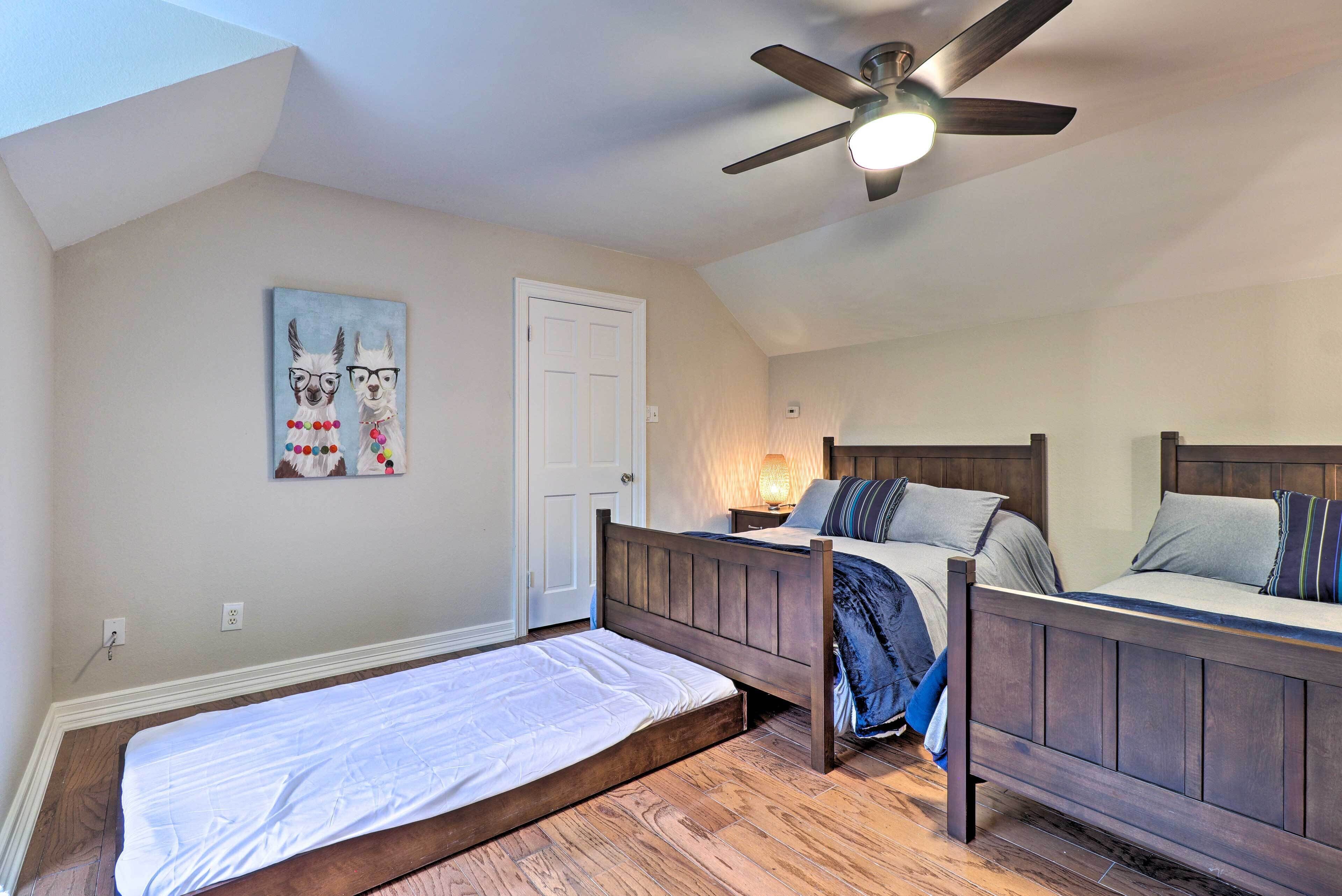 A bedroom with two beds, a ceiling fan, a painting, and a door.