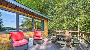 A wooden deck with wicker chairs and a picnic table, overlooking a body of water. - Lakefront Hideaway w/ Dock, Kayaks, Fire Pit! (Glennie)