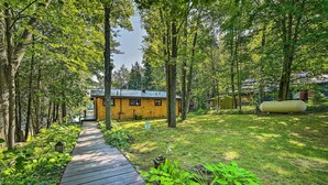 A wooden pathway leading to a yellow cabin surrounded by lush greenery and tall trees. - Lakefront Hideaway w/ Dock, Kayaks, Fire Pit! (Glennie)