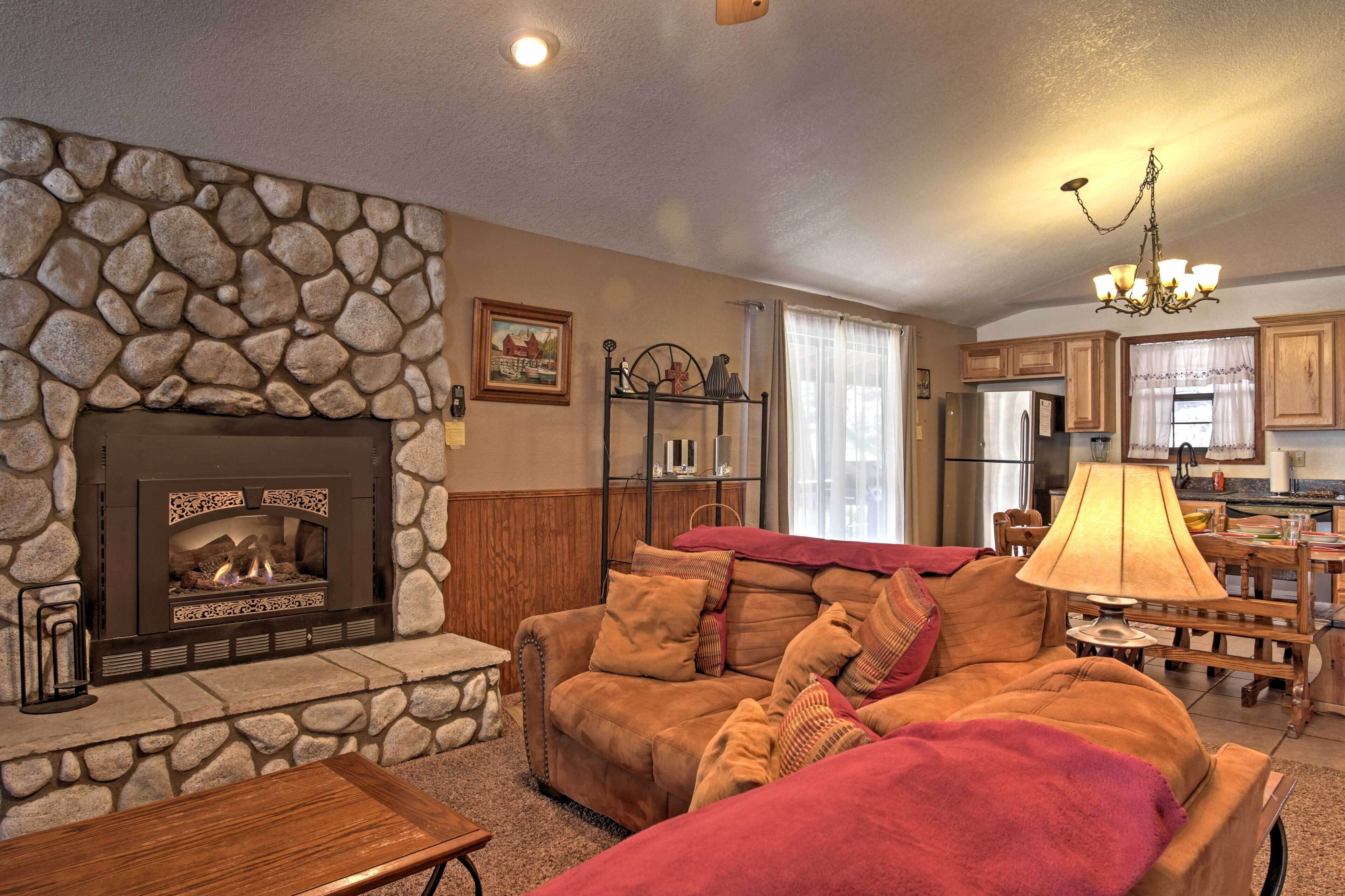 A cozy living room with a stone fireplace, a comfortable sofa, and a dining area with wooden furniture.
