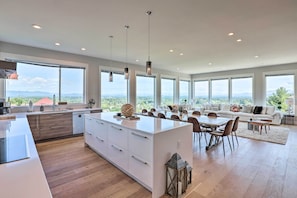 A spacious kitchen with a large island, dining area with a sofa, and large windows offering a view of the mountains. - Luxe Asheville Home w/ Stunning Mountain Views! (Asheville)