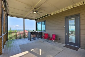 A covered outdoor area with a ceiling fan, a bar with stools, and two red chairs. - Luxe Asheville Home w/ Stunning Mountain Views! (Asheville)