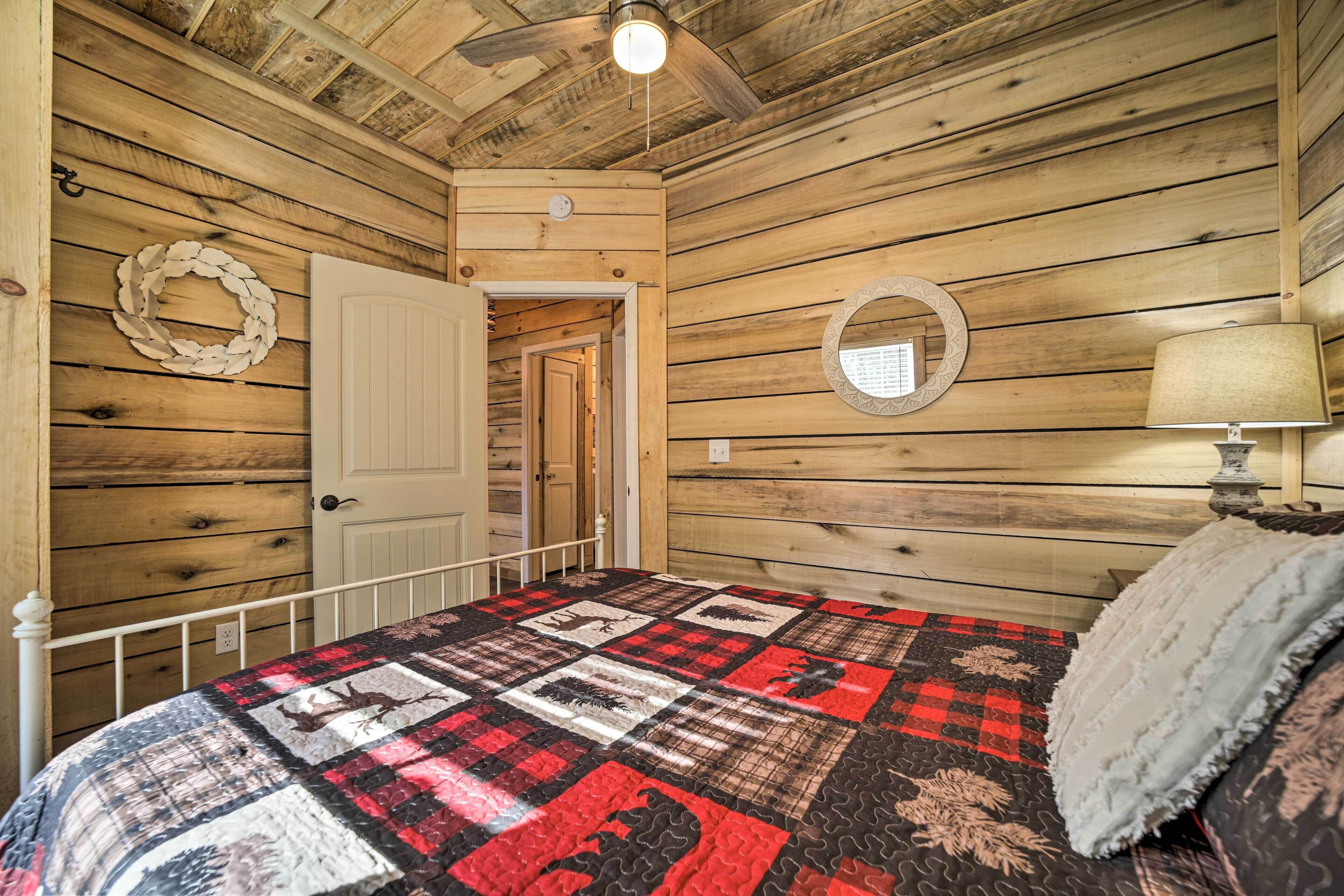 A wooden-paneled room with a bed, a white door, a wall clock, a round mirror, and a ceiling fan.