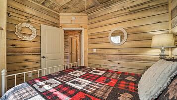 A wooden-paneled room with a bed, a white door, a wall clock, a round mirror, and a ceiling fan.
