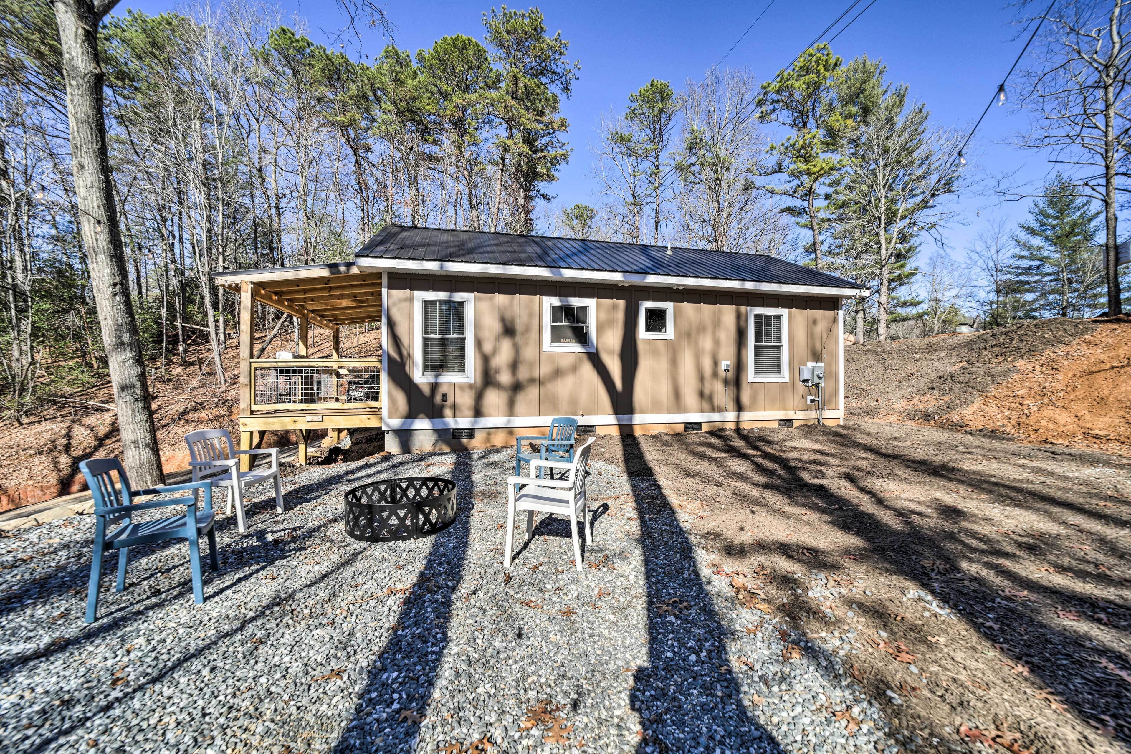 A small cabin with a covered porch, a gravel driveway, and a few chairs.