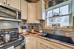 A kitchen with a stainless steel microwave, stove, and sink. There is a window with a view of trees and a sign above it. - Modern Cabin w/ Fire Pit < 3 Mi to Trails! (Pisgah Forest)